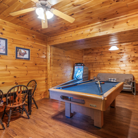 Game room of a Star Chase Cabin, showing a table and chairs, an overhead fan, a pool table, Skee-Ball, and a sofa